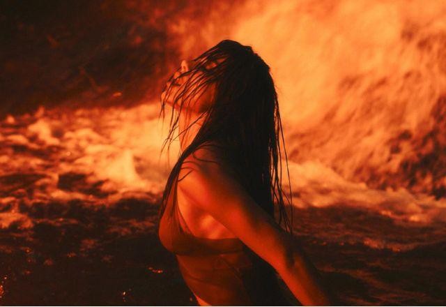 Anitta em uma cachoeira com uma luz amarelada, olhando pra cima, com cabelo molhado na frente do rosto dela